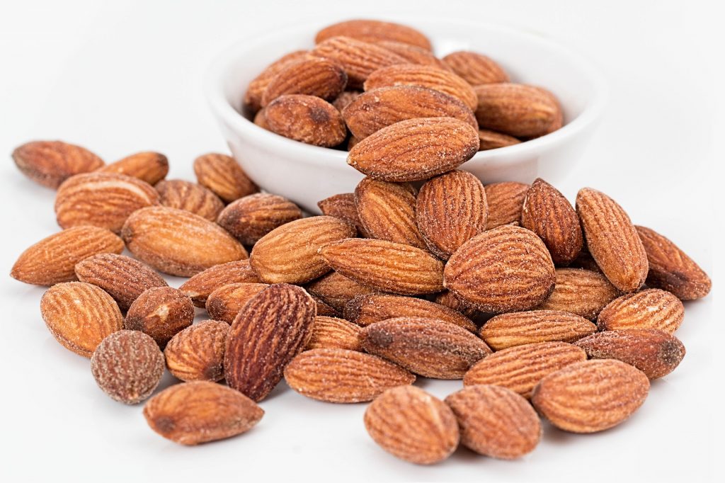 A close-up of almonds in a small bowl and piling onto a white countertop.