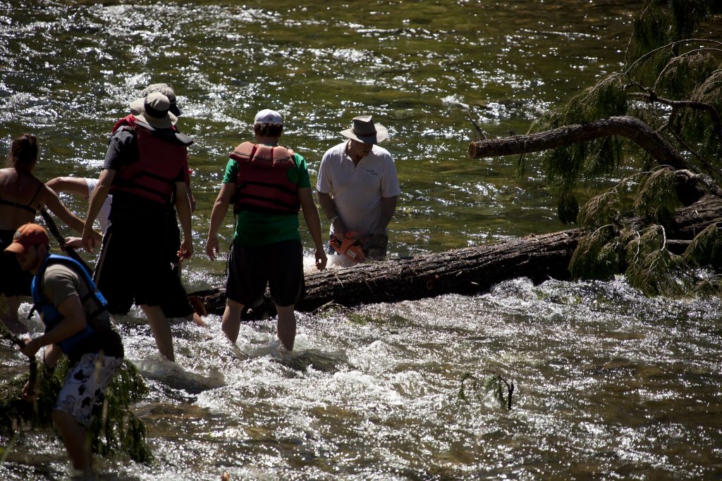 Gary Young chainsawing through a log in a river.