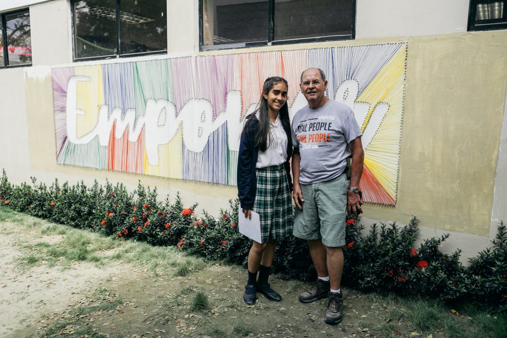 Two people, a young woman and an older man, stand in front of a wall decorated with the word "empower."
